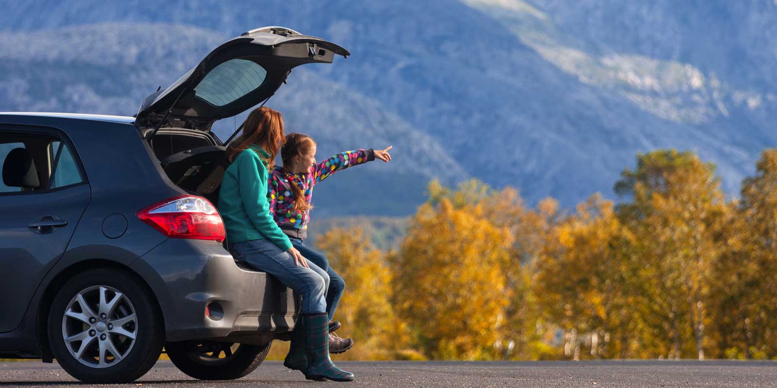 Mother and daughter sat in their car boot by the mountains