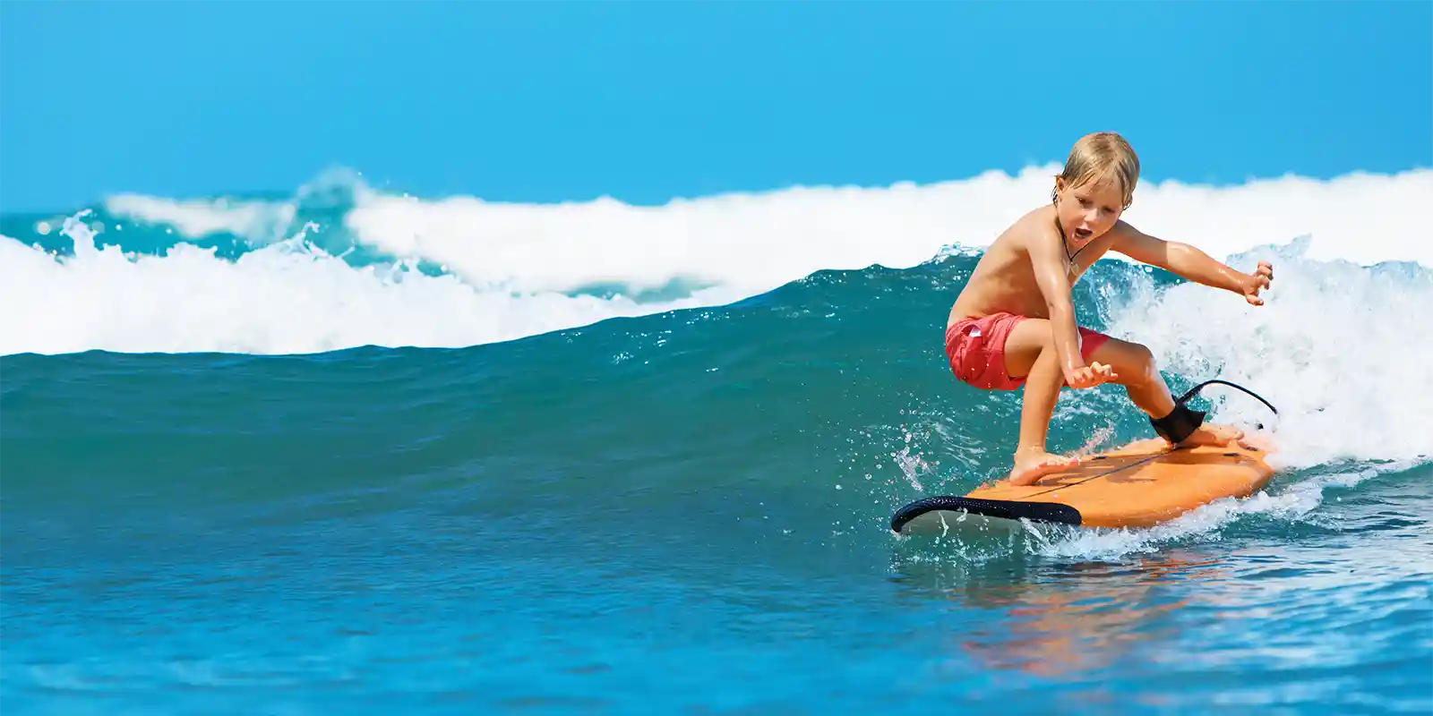 Boy surfing on bright blue waves and orange surfboard