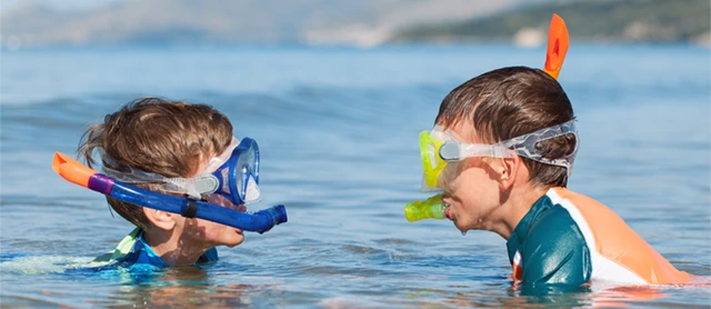 Siblings snorkelling, wearing masks and facing each other