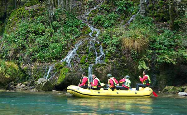 Group in inflatable raft on river with waterfall coming down cliff behind